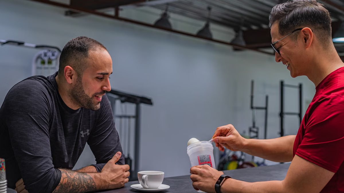 Side view of strong friends talking while preparing high protein smoothie after hard workout